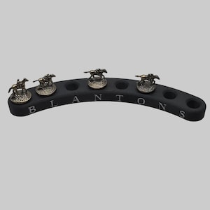 May include: Black, curved bar with five circular holes and the word "BLANTONS" engraved. Each end has a small, bronze-colored horse figurine. A unique bar accessory.