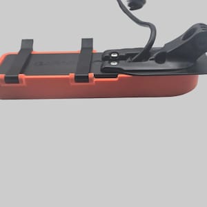 Può includere: Un ecoscandaglio Garmin arancione e nero con un cavo nero. Il dispositivo ha una base rettangolare arancione con cinghie nere e una sezione superiore nera. Il logo Garmin è visibile.