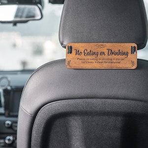 May include: Wooden sign with the text "No Eating or Drinking" hanging from a car headrest. The sign also includes the text "Please, no eating or drinking in the car. Let's keep it clean for everyone!"