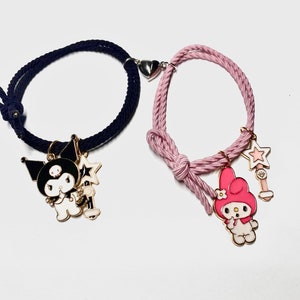 May include: Two matching friendship bracelets. One is navy blue, the other is pink. Each bracelet has a charm of a cartoon character and a star. The bracelets connect with a magnetic heart clasp.