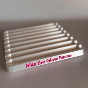 May include: White plastic tray with multiple slots for holding items. The tray has the words "Mila the Glow Nurse" printed in pink on the front.