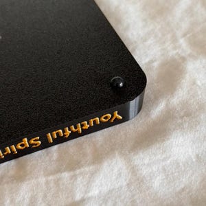 May include: Black rectangular object with a gold inscription that reads "Youthful Spirit".