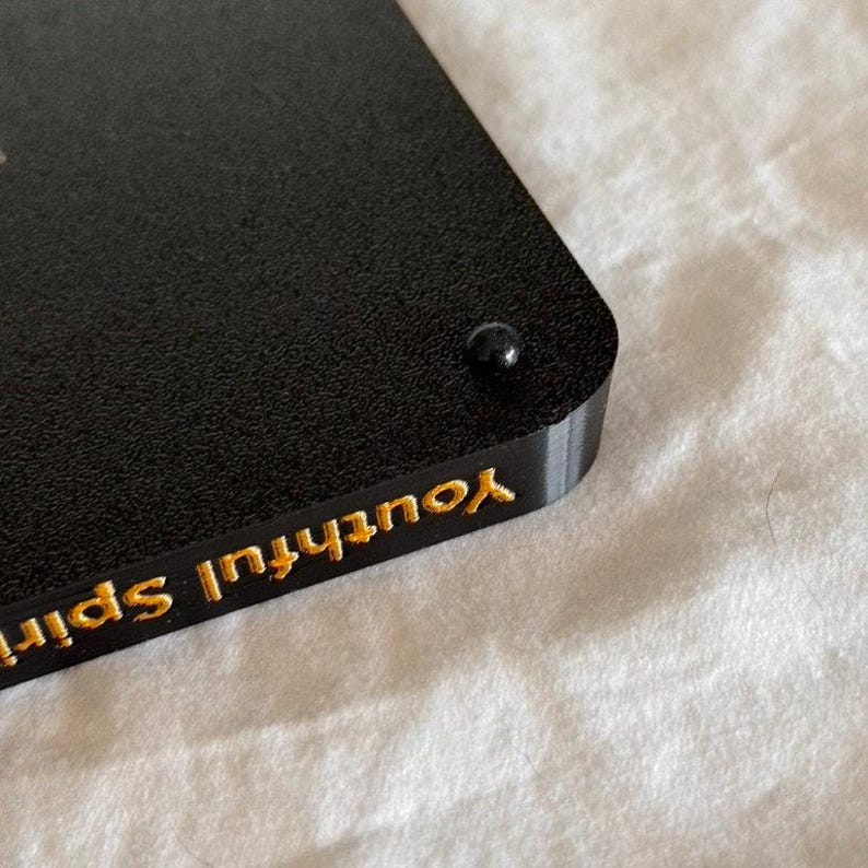 May include: Black rectangular object with a gold inscription that reads "Youthful Spirit".