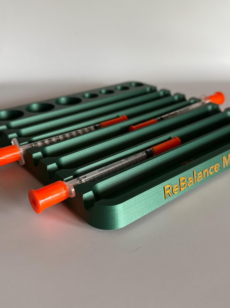 May include: A green plastic organizer with multiple slots for storing syringes. The organizer has the text "ReBalance" printed in gold on the side.
