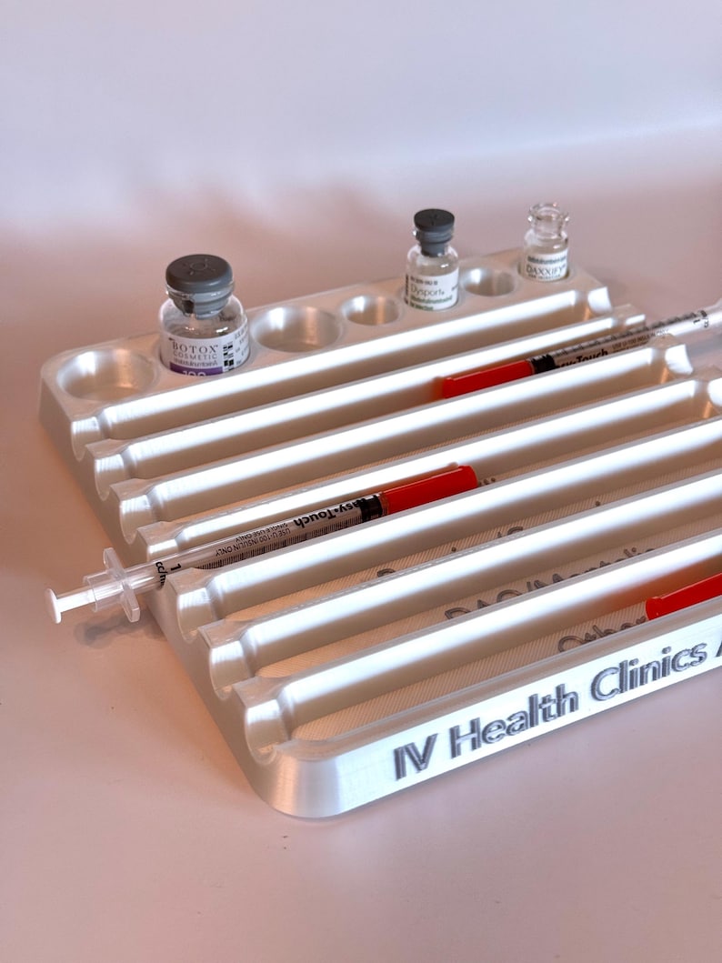 May include: White plastic tray with multiple compartments for vials and syringes. The tray has the text "IV Health Clinics" printed on the bottom. There are three vials and two syringes in the tray.