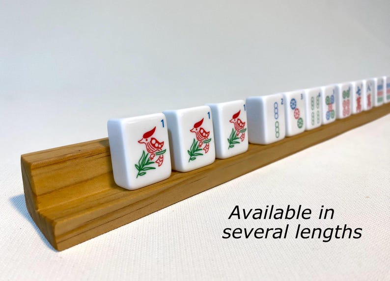 May include: A wooden rack for holding mahjong tiles. The rack is made of light brown wood and has a natural finish. The rack is designed to hold 14 tiles in a row. The rack is available in several lengths. The tiles are white with red and blue designs.