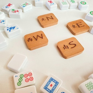 May include: A collection of Mahjong tiles, including wooden direction tiles marked with "N", "E", "S", and "W". White tiles with various symbols and characters are scattered around the wooden tiles.