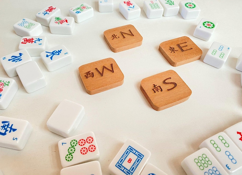 May include: A collection of Mahjong tiles, including wooden direction tiles marked with "N", "E", "S", and "W". White tiles with various symbols and characters are scattered around the wooden tiles.
