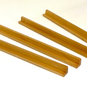 May include: Four wooden tile racks, each with a U-shaped groove, are arranged in a staggered pattern on a white surface.