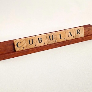以下が含まれることがあります： 木製のラックに「CUBULAR」という単語が文字タイルで綴られています。各タイルには、ゲームでのポイント値を示す数字が書かれています。