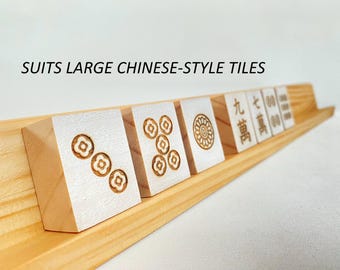 May include: A light-colored wooden rack holding several white Mahjong tiles with engraved floral and numerical designs. The text SUITS LARGE CHINESE-STYLE TILES is visible above the rack, which features a slanted design for tile display.