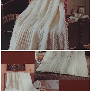 Op de afbeelding: Een wit gebreid babydekentje met een delicate kantzoom en ingewikkelde patronen. Het dekentje is over een stoel en een tafel gelegd met een kleine vaas en een boek.