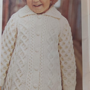 May include: A white knitted cardigan with a cable knit pattern and button fastening. The cardigan has a collar and long sleeves.