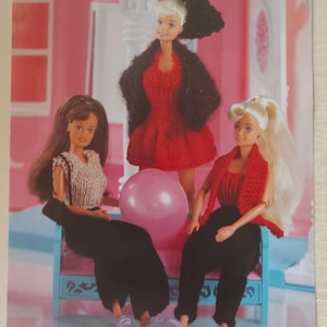May include: A knitting pattern for three doll outfits. The outfits are a red dress with a black jacket, a grey top with black trousers, and a red top with black trousers. The pattern is called "Fashion Doll Outfits" and is from Waterwheel.