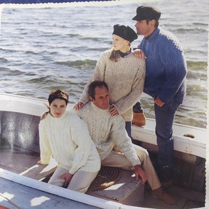 Puede incluir: Cuatro personas con suéteres están sentadas en un bote en el agua. Los suéteres son de punto Aran en 8 cabos. El texto "Aran Handknits in 8 ply" es visible en la imagen.
