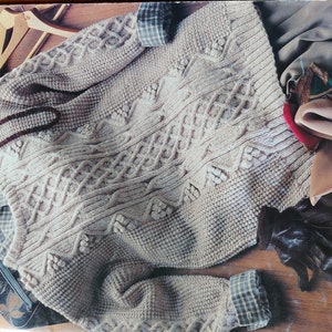 May include: A cream-colored knitted sweater with a cable knit pattern. The sweater has a V-neck and is made with a thick yarn.