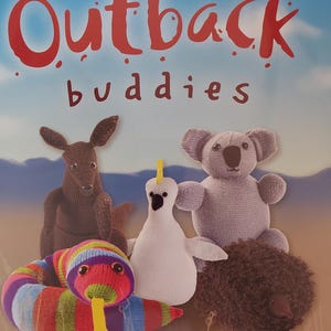 May include: A book titled "Outback Buddies" with a colorful illustration of five knitted animal toys. The toys include a kangaroo, a koala, a snake, a bird, and a hedgehog.