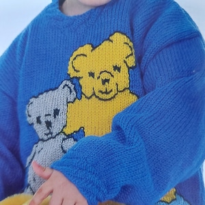 May include: A blue knitted sweater with a yellow and gray teddy bear design. The sweater has a crew neck and long sleeves.