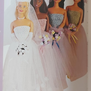 May include: Four Barbie dolls dressed in knitted wedding attire. The bride is wearing a white dress with a veil, while the bridesmaids wear pink, blue, and green dresses. Each doll holds a bouquet of flowers.