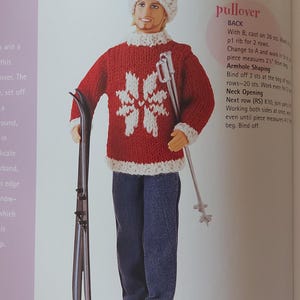 May include: A doll wearing a red and white snowflake-patterned sweater and matching hat, with blue jeans and skis. The word "Pullover" is visible in the image.