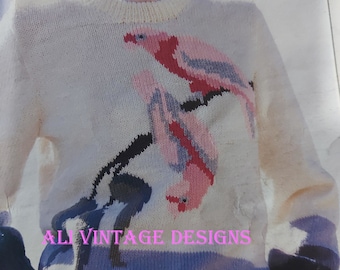 May include: Cream-colored knit sweater featuring a bird design in pink, red, and blue. The sweater has a crew neck and long sleeves with blue and black cuffs. The text "AL VINTAGE DESIGNS" is printed on the sweater.