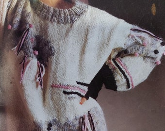 May include: A white knitted sweater with pink, black, and gray accents. The sweater has a loose fit and a crew neck. The sweater is made with Patons Overlander 12ply yarn.