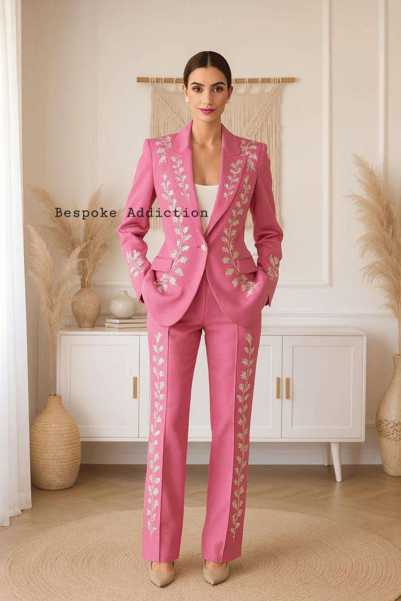 May include: A pink suit with floral embroidery. The suit includes a blazer with pockets and matching pants. The text "Bespoke Addiction" is visible on the image. The outfit is worn with nude heels.