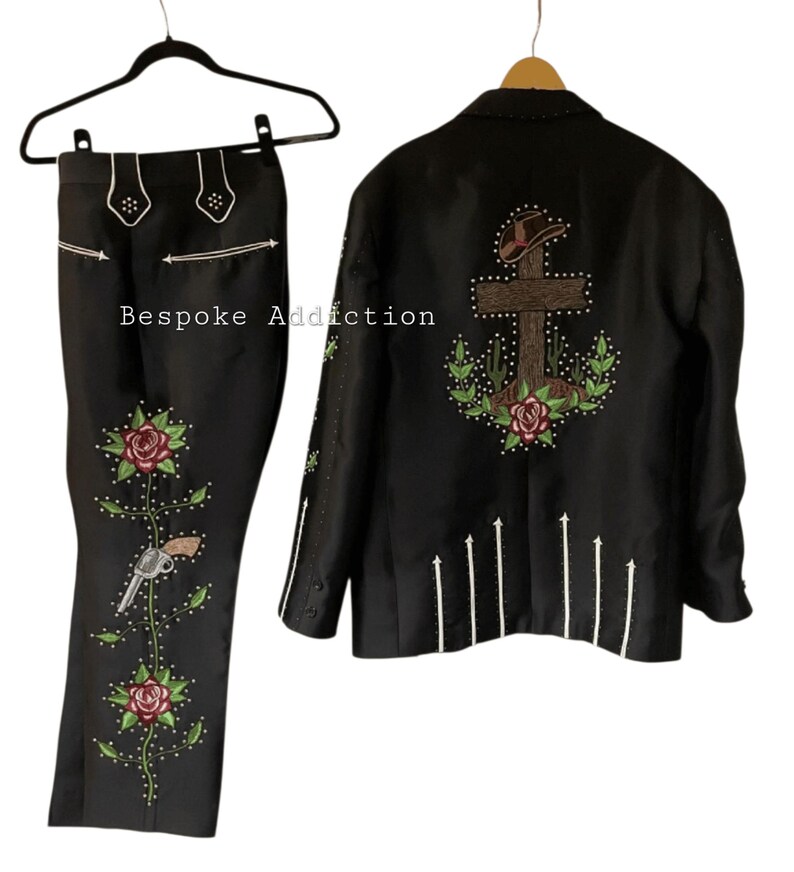 Puede incluir: Traje negro de estilo western con intrincados bordados. La chaqueta presenta un dise&ntilde;o de cruz y cactus en la espalda, mientras que los pantalones tienen motivos florales y de pistola. El texto "Bespoke Addiction" es visible.