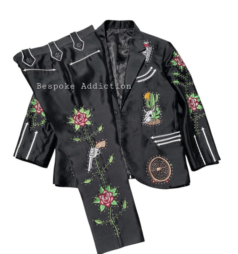 Puede incluir: Traje negro con bordados florales, cactus y pistola. La chaqueta y el pantal&oacute;n presentan detalles blancos y el texto "Bespoke Addiction". El traje tiene un acabado satinado.