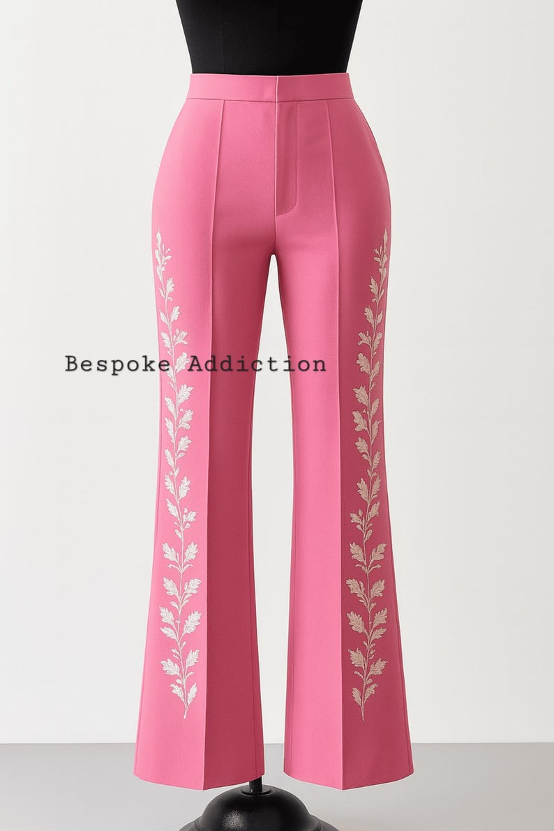 May include: Pink high-waisted pants with a flared leg. The pants feature a white leaf design on the sides and the text "Bespoke Addiction". The pants are displayed on a mannequin.