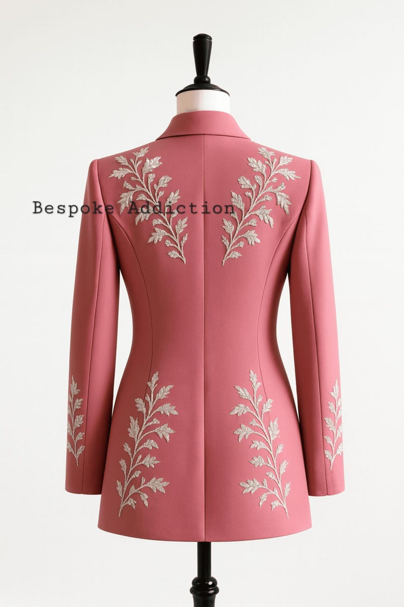May include: A dusty rose blazer with intricate silver leaf embroidery on the back and sleeves. The text "Bespoke Addiction" is visible on the back of the blazer. The blazer is displayed on a mannequin.