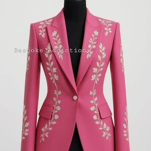May include: A vibrant pink blazer with intricate floral embroidery. The jacket features a single-button closure, two front pockets, and long sleeves. The text "Bespoke Addiction" is visible on the left side. This tailored blazer is a stylish addition to any wardrobe.