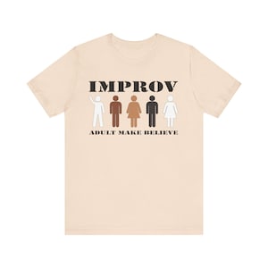 May include: Beige t-shirt with the word "IMPROV" in black block letters above stick figures of different skin tones. Below the word "IMPROV" is the phrase "ADULT MAKE BELIEVE" in black block letters.