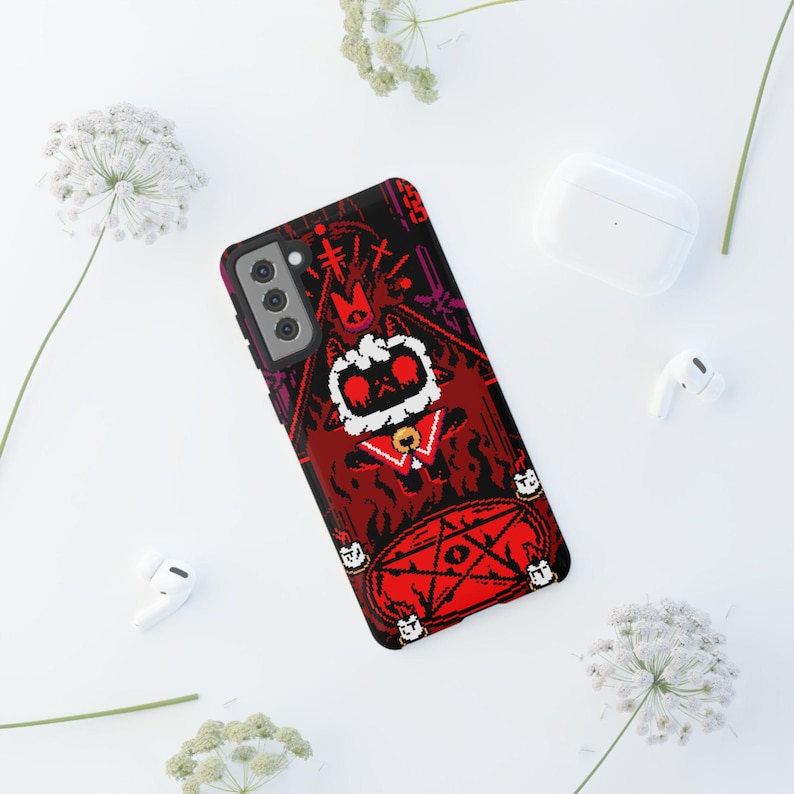 Op de afbeelding: Een rode, zwarte en witte telefoonhoes met een pixelontwerp van een kat met een kroon die voor een pentagram staat. De kat wordt omringd door vlammen en kaarsen.