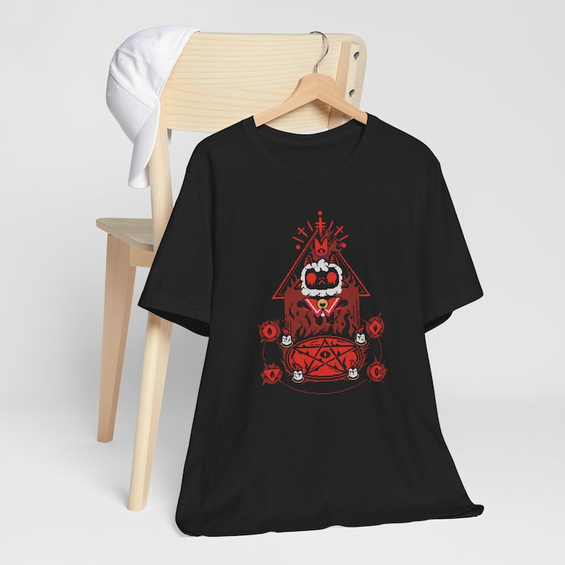 May include: Black t-shirt with a red graphic design of a cartoon character wearing a crown and sitting on a pentagram. The character is surrounded by red symbols and the text "M.C.C."