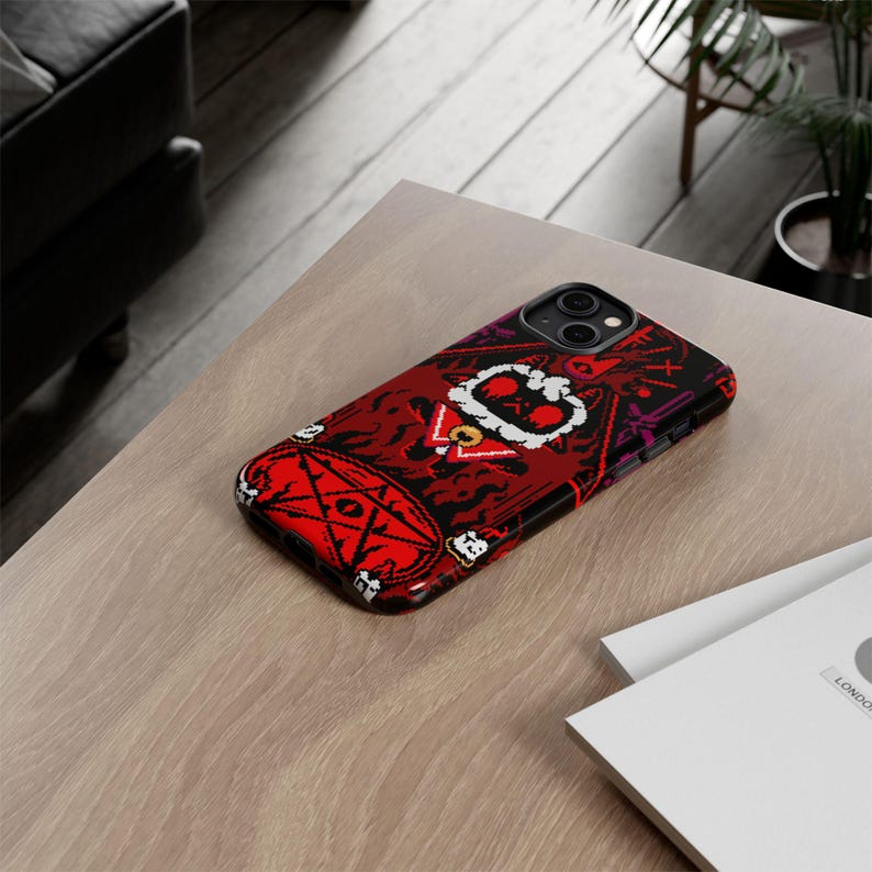 Op de afbeelding: Een rode, zwarte en witte telefoonhoes met een pixelontwerp van een wezen met een kroon en een pentagram. De hoes is ontworpen voor een iPhone.