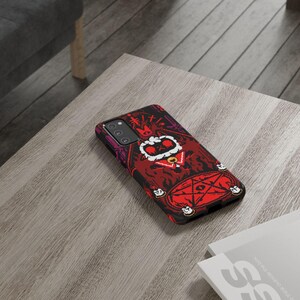 Op de afbeelding: Een zwarte telefoonhoes met een rode, zwarte en witte illustratie van een cartoonfiguur met een kroon en een staf. Het figuur is omringd door een pentagram en kaarsen. De hoes heeft een camera-uitsparing en een uitsparing voor de knoppen van de telefoon.