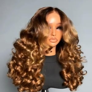 Peut inclure: Perruque bouclée marron et blonde coiffée sur une tête de mannequin. La perruque présente de longues boucles volumineuses avec un mélange de reflets brun clair et blond doré. Le mannequin porte un haut noir.