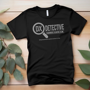 May include: Black t-shirt with a white graphic design that says "DX DETECTIVE DIAGNOSES SLEUTHS CLUB" and "Solving documentation mysteries one chart at a time".