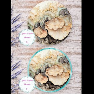 May include: Two round coasters with a design of beige and brown mushrooms on a white background. The top coaster has a plain edge, while the bottom coaster has a teal blue edge.