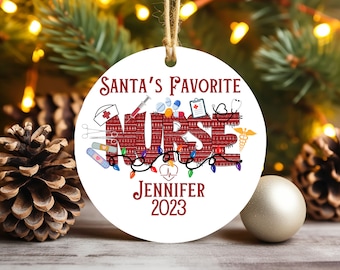 May include: White round Christmas bauble with red and white text that reads "Santa's Favourite Nurse" with a red and white knitted pattern. The bauble also features a red heart with a stethoscope and the text "Jennifer 2023".