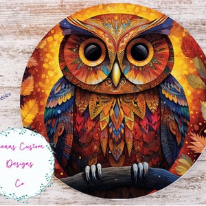 May include: A colorful owl with intricate patterns and feathers, set against a background of autumn leaves. The owl's eyes are large and black, and its beak is yellow. The owl is perched on a branch.