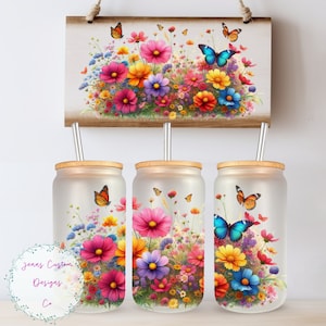 May include: Three frosted glass tumblers with a floral design featuring pink, yellow, and purple flowers, green leaves, and blue and orange butterflies. Each tumbler has a bamboo lid and a clear straw.