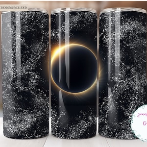 May include: Three stainless steel tumblers with a black and white galaxy design. The centre tumbler features a solar eclipse with a bright yellow halo.