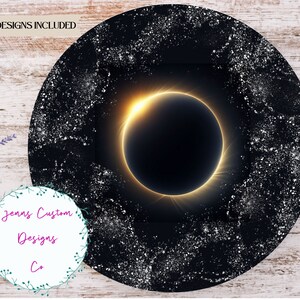 May include: A round design in black and gold featuring a solar eclipse image. The design has a white background with a black and gold circle in the centre. The circle contains a black eclipse image with a gold halo. The background is covered in white dots.