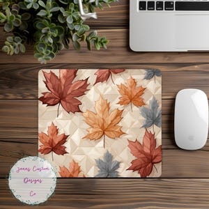 Może przedstawiać: Podkładka pod mysz z geometrycznym wzorem przedstawiającym kolorowe jesienne liście w odcieniach czerwieni, pomarańczy i brązu. Liście są ułożone w powtarzający się wzór na kremowym tle.