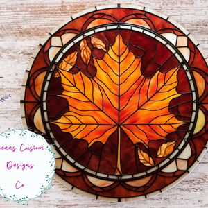 May include: A stained glass round panel featuring a large orange and red maple leaf with smaller leaves around it. The panel is set in a brown frame with a decorative border.