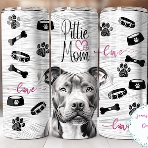 Puede incluir: Un vaso blanco con una imagen en blanco y negro de un perro pit bull. El vaso tiene un fondo de madera con huellas de patas, huesos, collares y cuencos para comida. El texto "Pittie Mom - Love" está impreso en el vaso.