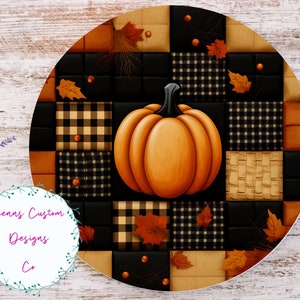 May include: A round, orange pumpkin with a green stem sits in the center of a patchwork design. The design features black and white checkered squares, brown squares, and orange squares with brown leaves.