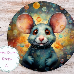 Peut inclure: Illustration circulaire d'une souris bleue aux grandes oreilles et aux yeux bruns, entourée de bulles colorées. La souris a un nez rose et sourit. Le fond mélange des teintes orange, jaune et bleu. Le texte "Jennas Custom Designs Co" est visible.